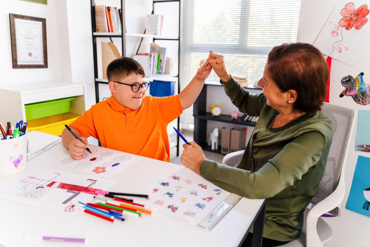 A boy with down syndrome is high five in a classroom with his teacher